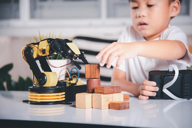 Happy Asian little kid boy using remote control playing robotic machine arm for pick up wood block