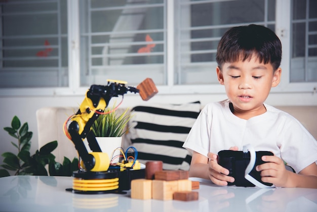 Happy Asian little kid boy using remote control playing robotic machine arm for pick up wood block