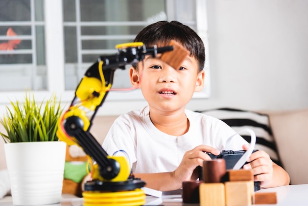 Happy asian little kid boy using remote control playing robotic machine arm for pick up wood block