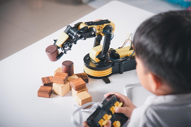 ウッドブロックを拾うためにロボットマシンアームを再生するリモコンを使用して幸せなアジアの小さな子供の男の子