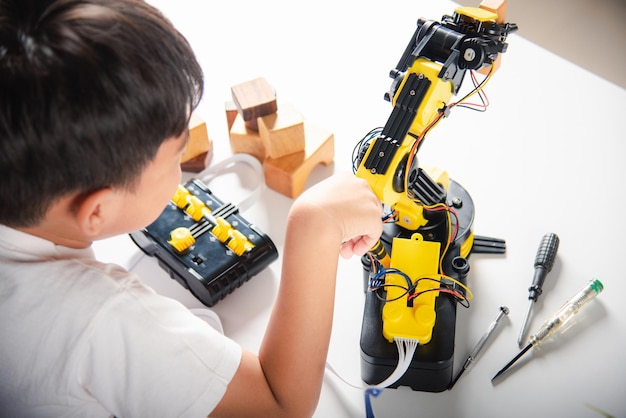 Happy Asian little kid boy using screwdriver to fixes screws robotic machine arm in home workshop