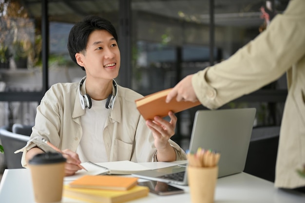 幸せなアジアの男子大学生は、カフェで友人と話し、学校のプロジェクトを行っています