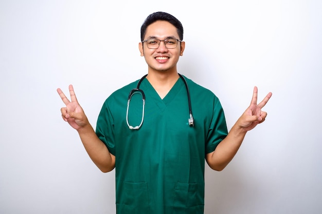 平和かわいいジェスチャーを示し、病院での仕事中に前向きな笑顔を見せるスクラブで幸せなアジアの男性医師看護師