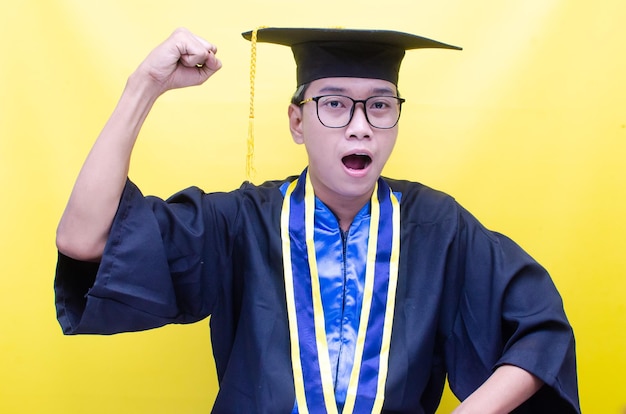 卒業式の制服の帽子とガウンを着た幸せなアジアの男子学生がポーズをとり、彼の業績を祝う