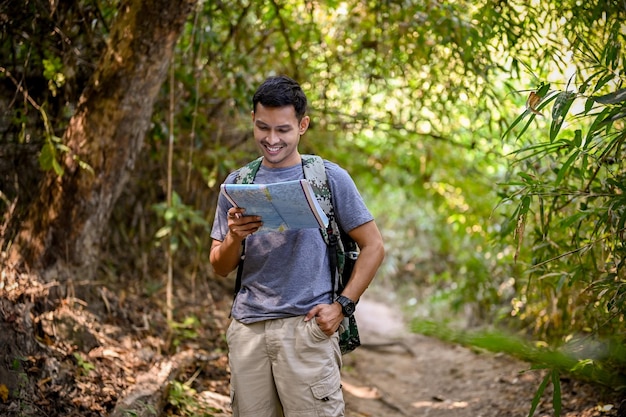 Happy Asian male trekker looking at the trekking route on the map enjoys walking the trail