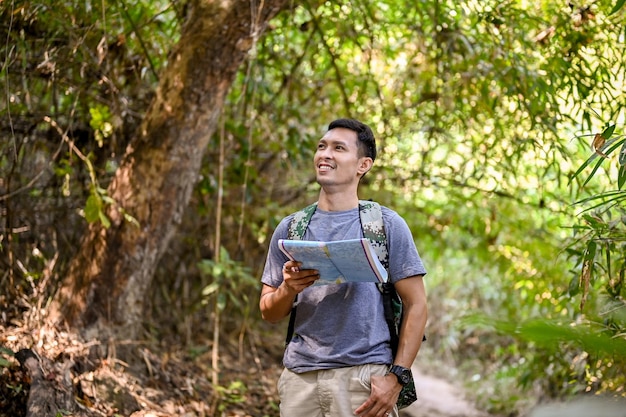 美しい自然の景色を見て地図を持っている幸せなアジア人男性トレッカーまたは旅行者