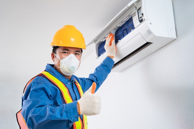 幸せなアジア人男性は、防塵技術者が室内でエアコンを掃除するのを防ぐために安全マスクを着用します、エアコン技術者
