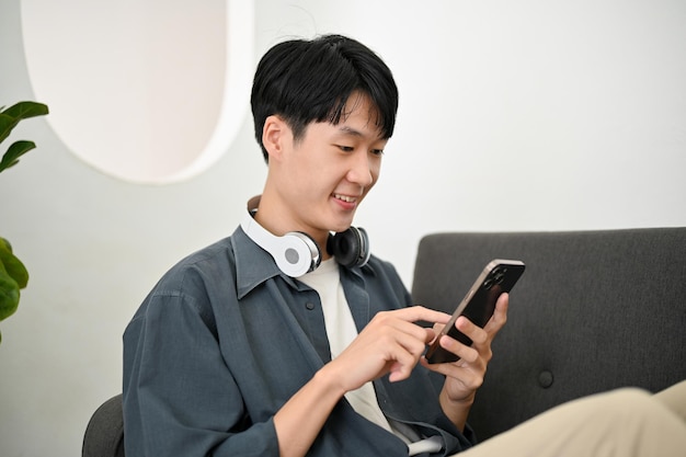 Happy Asian man chatting with his friends on the phone while chilling on sofa in his living room