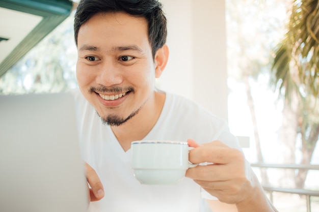 Happy Asian man drink coffee while working with computer.