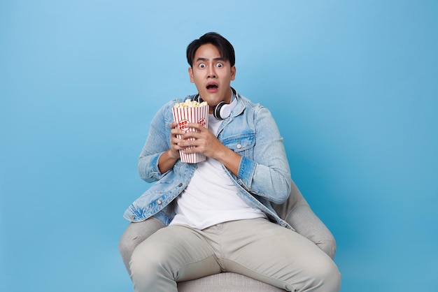 Фото Счастливый азиатский мужчина ест попкорн и в ужасе, сидя и смотря фильм в кинотеатре