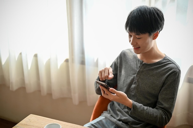 幸せなアジア人男性は、カフェでくつろぎながら電話で友達とおしゃべりを楽しんでいます