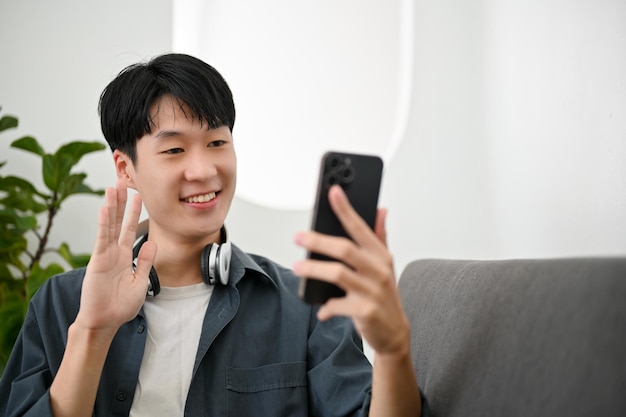 Happy asian man enjoys talking on video call with his friend\
while relaxing in the living room