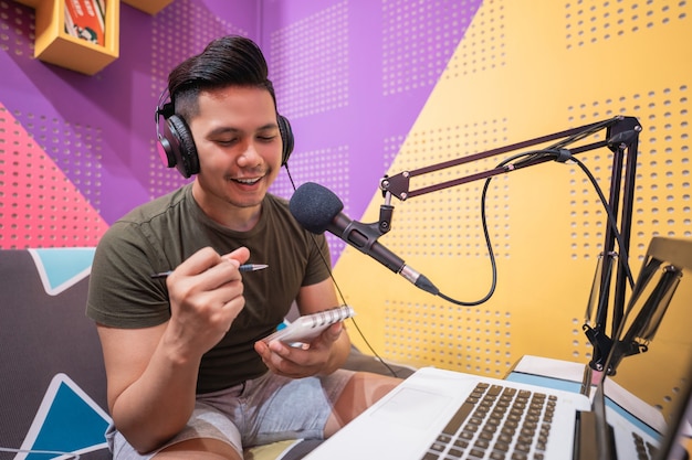 Happy asian man is recording a podcast in his studio take note