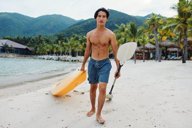 Happy asian man kayaking in tropical paradise exhilarating recreational adventure on beach with