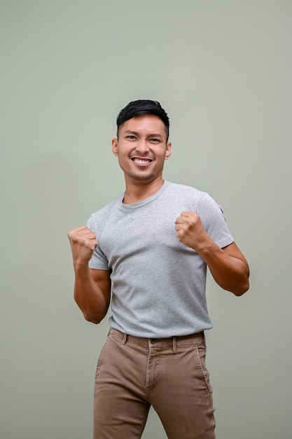 Happy Asian man raising hands up rejoicing yes gesture winning victory celebrating