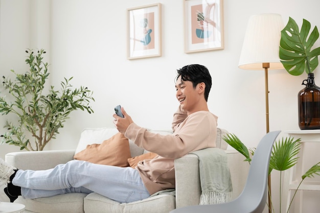 A Happy asian man sitting on couch using smartphone in living room at home