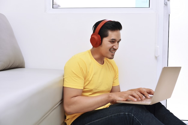 Uomo asiatico felice che si siede con il computer portatile e le cuffie