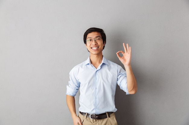 Happy asian man standing isolated, showing ok