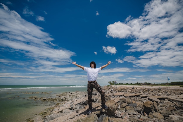 写真 青い空と岩のビーチに立っている幸せなアジア人