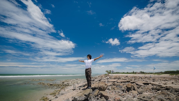 Happy asian man standing on the rock beach with blue sky