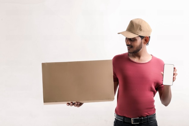Счастливый азиатский мужчина в футболке и кепке держит пустую коробку, изолированную на белом фоне, концепция службы доставки