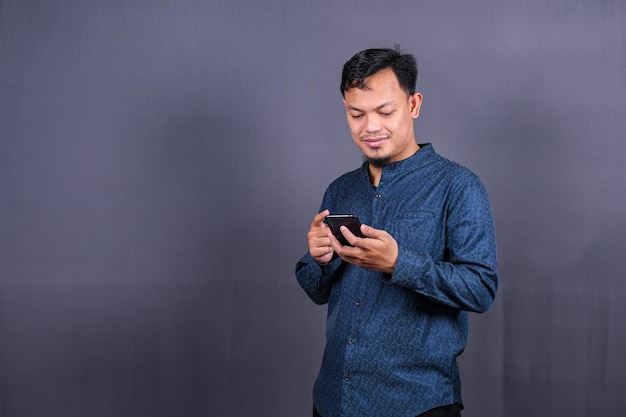 Happy asian man typing sms on gray background. isolated, business concept