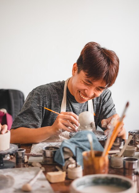 Happy asian man working in pottery studio ceramic artist makes\
classes of hand building in modern pottery workshop creative people\
handcrafted design