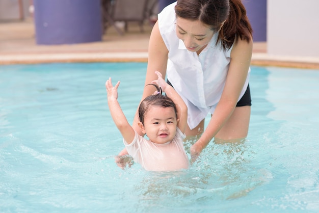 A Happy Asian mother and daughter are enjoy swimming in pool , lifestyle, parenthood, family concept