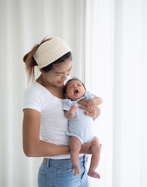 Happy Asian mother holding a lovely newborn baby in kids bedroom woman mother hugging her newborn baby standing by the window