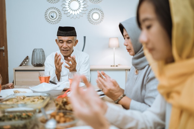 Photo happy asian muslim family praying before having their iftar meal during ramadan fasting