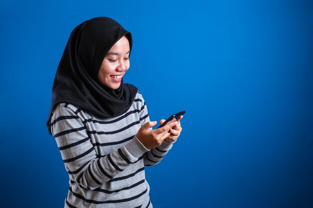 happy asian muslim girl smiling while browsing trough internet or reading chat message on her phone