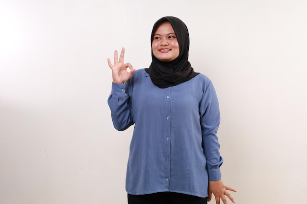 Happy asian muslim woman standing looking sideways while making okay hand gesture