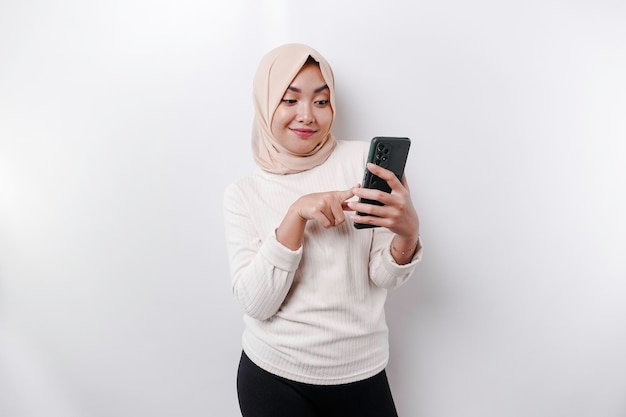 A happy Asian Muslim woman wearing a headscarf holding her phone isolated by white background