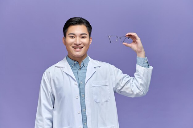 Happy asian ophthalmologist doctor holding glasses recommending to improve eyesight looking at camera