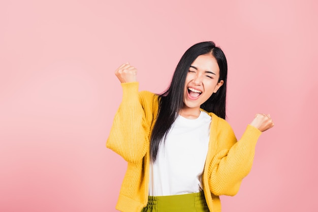 Happy Asian portrait beautiful cute young woman standing winning and surprised excited screaming open mouth raise hands, studio shot isolated pink background, Thai female wow with copy space