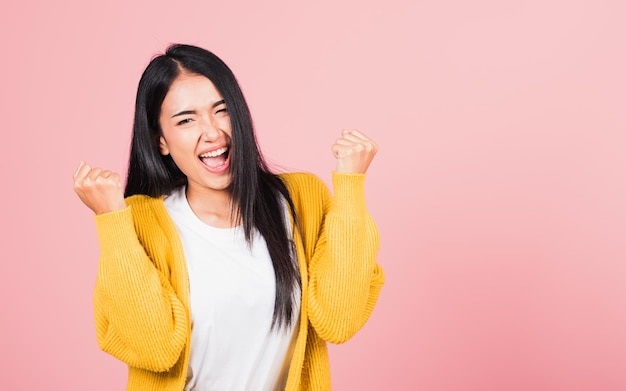 Happy Asian portrait beautiful cute young woman standing winning and surprised excited screaming open mouth raise hands, studio shot isolated pink background, Thai female wow with copy space