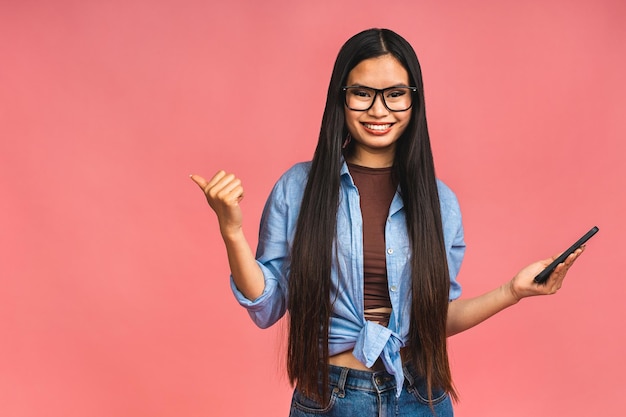 Happy Asian portrait beautiful cute young woman teen smiling excited typing text message on smart mobile phone enjoys online communication isolated on pink background with copy space