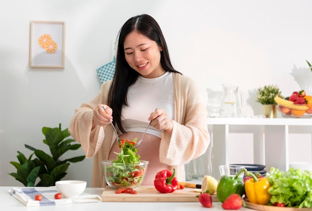 Счастливая азиатская беременная женщина готовит салат дома, делает свежий зеленый салат, ест много разных овощей во время беременности концепция здоровой беременности