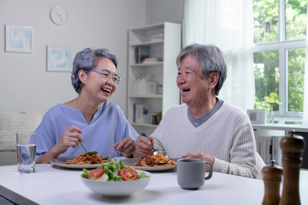 Happy asian senior couple eating meal together in kitchen at\
home retirement senior couple lifestyle living concept