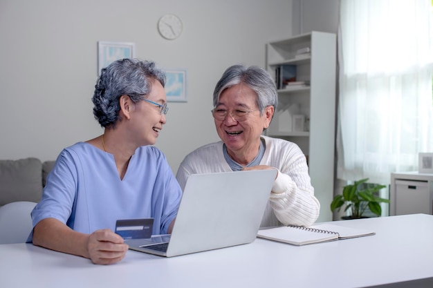 Happy asian senior couple at home handsome old man and\
attractive old woman are spending time together elderly couple with\
laptop and credit card in hands online shopping