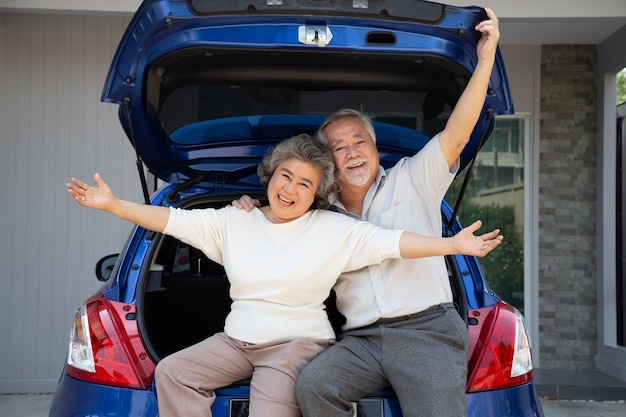 Happy Asian senior couple standing in back of the car and enjoying journey trip.