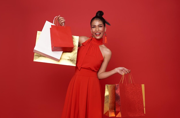 Happy Asian shopaholic woman wearing red dress showing shopping bag in shopping center