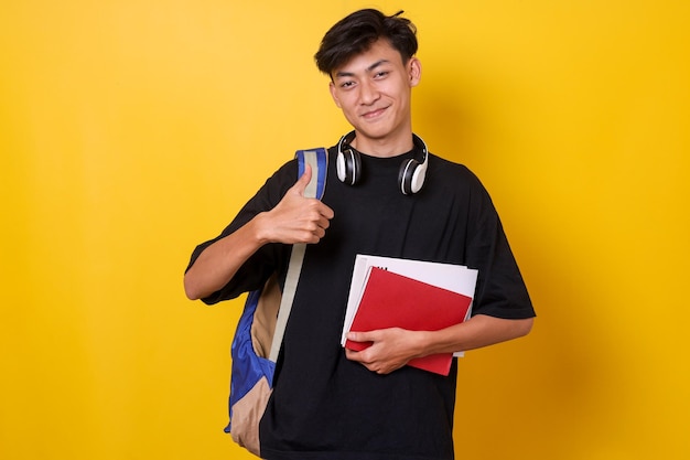 Happy asian student carrying backpack and holding books showing thumb up