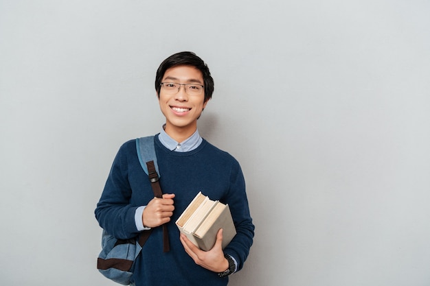 バックパックで幸せなアジアの学生。と本で。カメラを見て