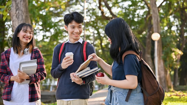 幸せなアジアの学生は、学校の公園を歩きながら、一緒に話したり笑ったりするのを楽しんでいます