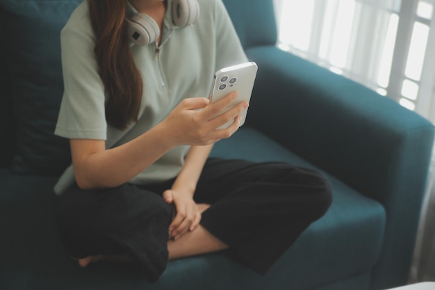 Happy Asian teen girl holding pad computer gadget using digital tablet technology sitting on the couch at home Smiling young woman using apps shopping online reading news browsing internet on sofa