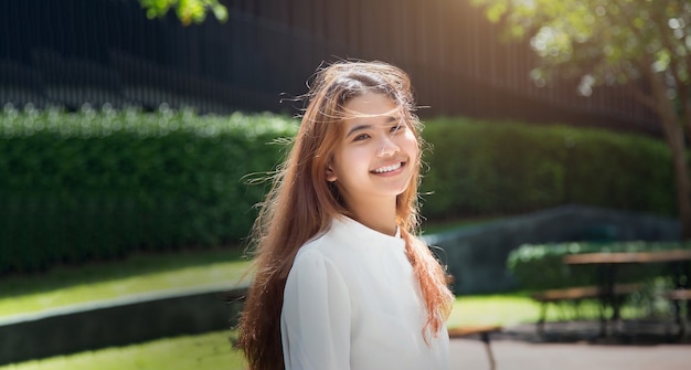 Sorriso asiatico felice della donna adolescente al parco all'aperto della macchina fotografica nella giornata di sole