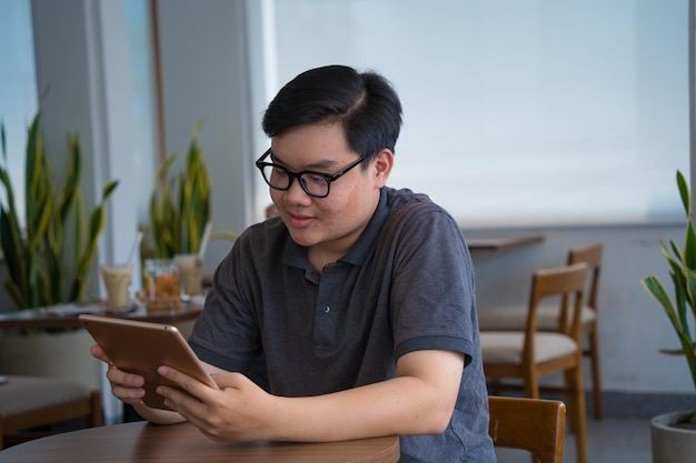 Happy Asian teenager using smart phone and tablet at coffee shop Asian man holding tablet call mom