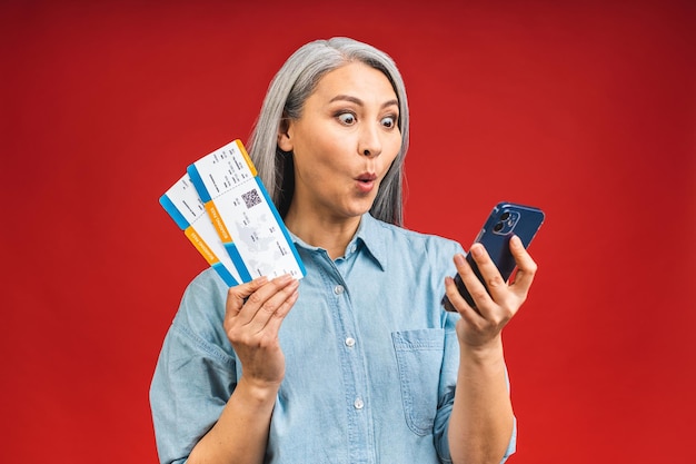 Happy asian traveler tourist elderly mature senior woman holding tickets isolated on red background studio Passenger travel abroad on weekends Using mobile phone