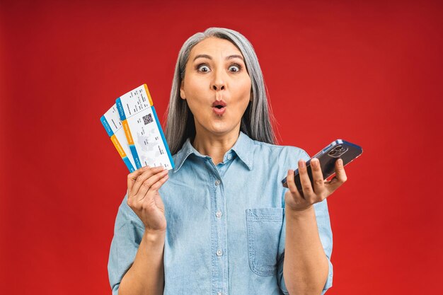 Happy asian traveler tourist elderly mature senior woman holding tickets isolated on red background studio Passenger travel abroad on weekends Using mobile phone